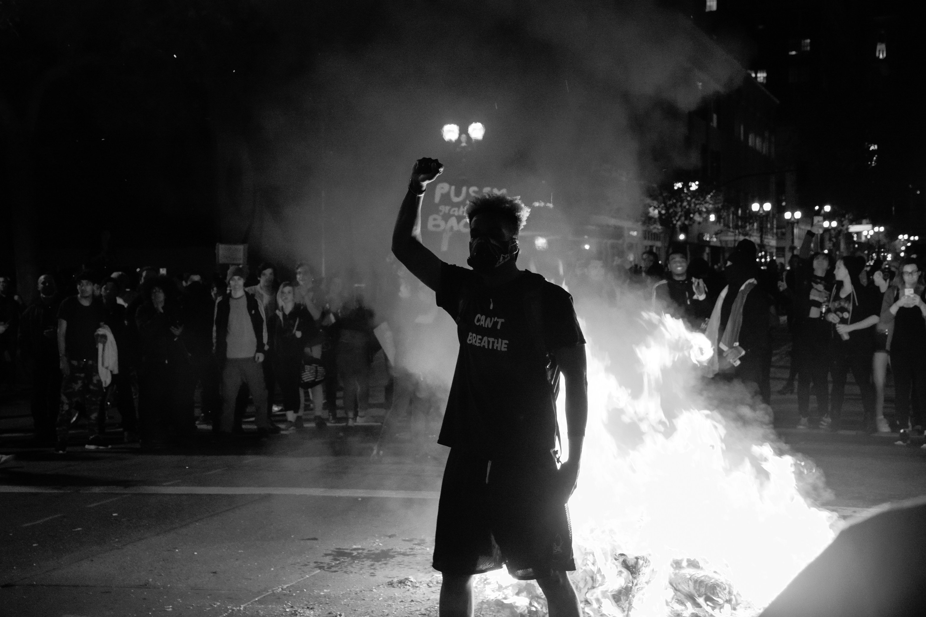 Man stands amid a protest with fist raised in the air. His shirt reads "I Can't Breathe."