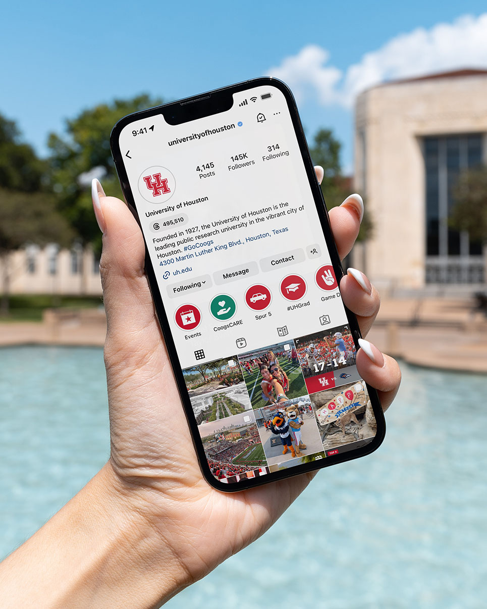 Close-up of a hand holding a phone with the UH Instagram account on its screen.