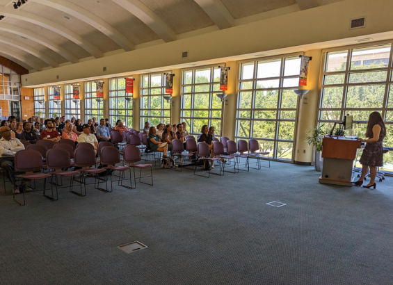 Dozens of people listen to a speaker in a large meeting space