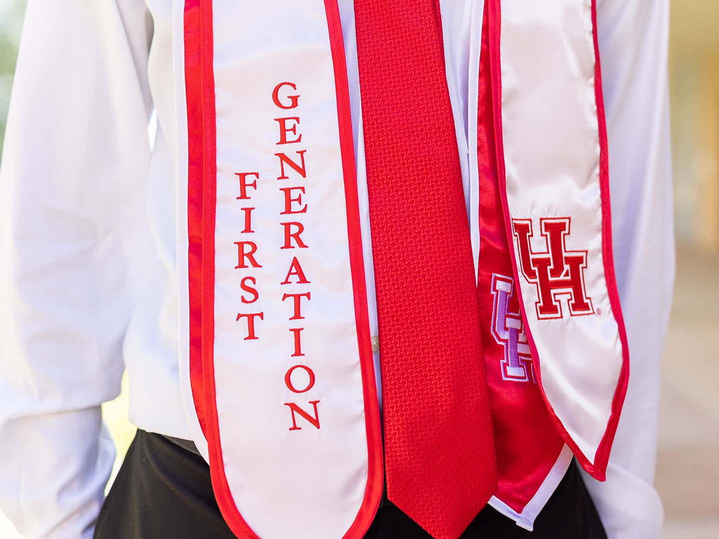 A student wearing a graduation stole that read “First Generation,” while donning a red tie and a University of Houston logo visible on the attire.