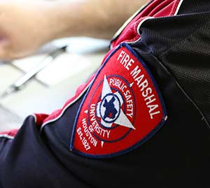 Close up of the left arm of red and black polo short. A badge on the sleeve says, "Fire Marshall. Public Safety".