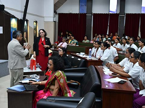 An Indian man and woman stand infrom for a lecture room filled with students.